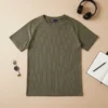 Camiseta Bershka verde oliva de segunda mano, manga corta raglán, tejido waffle acanalado, extendida sobre fondo beige con accesorios como reloj plateado, auriculares negros y libreta.