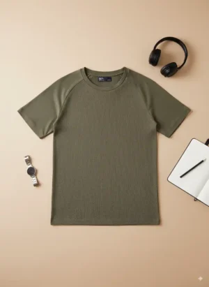 Camiseta Bershka verde oliva de segunda mano, manga corta raglán, tejido waffle acanalado, extendida sobre fondo beige con accesorios como reloj plateado, auriculares negros y libreta.